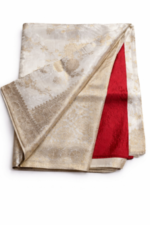 Luxurious ivory Banarasi silk saree adorned with intricate gold zari weaving, a regal border, and a striking contrast red blouse piece for timeless festive elegance.