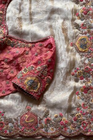 A luxurious peach beige designer organza saree featuring exquisite floral embroidery, scalloped embellished border, and a richly embroidered contrast pink blouse for regal occasion wear.