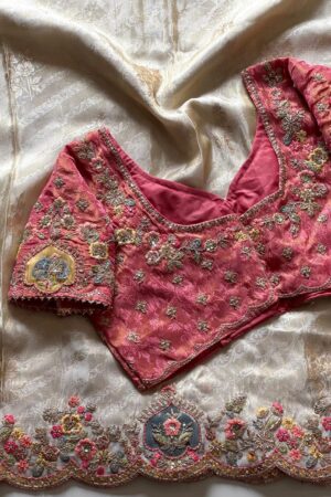 A luxurious peach beige designer organza saree featuring exquisite floral embroidery, scalloped embellished border, and a richly embroidered contrast pink blouse for regal occasion wear.