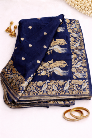 Elegant navy blue Banarasi soft silk saree featuring delicate silver buti motifs and a stunning floral bird woven border for a rich designer festive look.