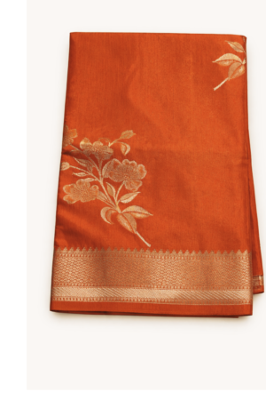 Striking burnt orange raw mango silk saree adorned with elegant floral silver zari motifs and a refined woven border for timeless festive charm.